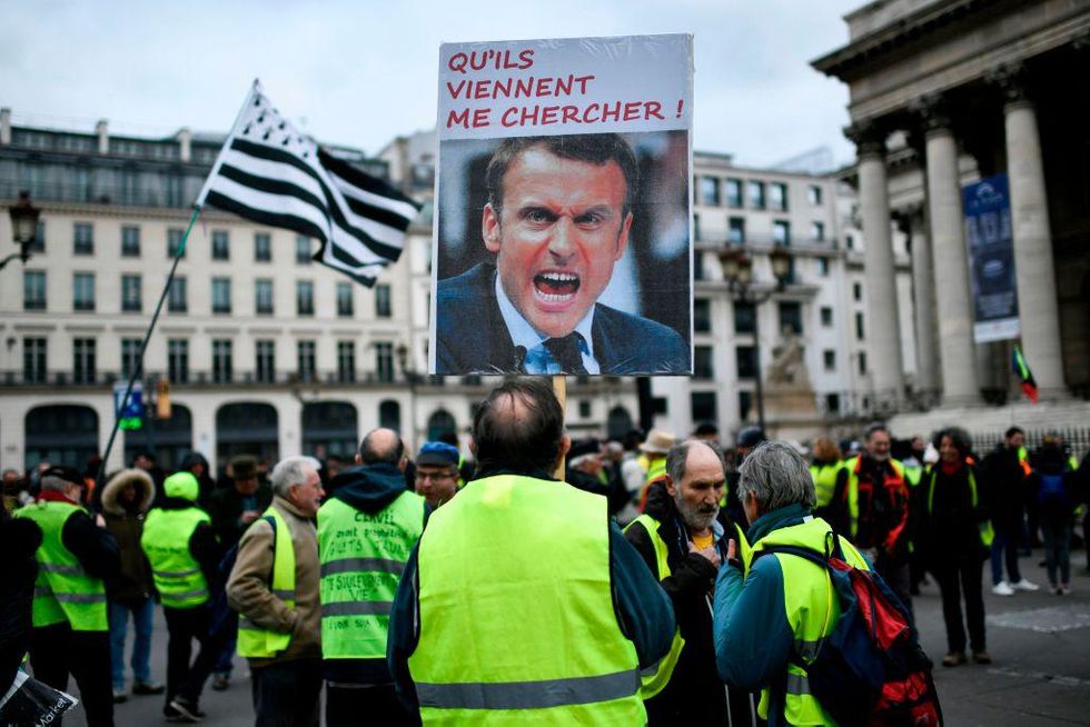 A protester holds a sign depicting French President and reading "Let them come and get me!" on the Place de la Bourse in Paris during a demonstration called by the "Gilets Jaunes" (Yellow Vests) movement on December 28, 2019, as part of a nationwide multi-sector strike against French government's pensions overhaul.