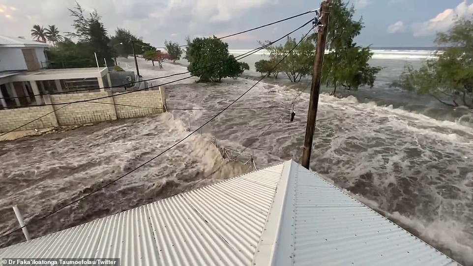 A tsunami has struck Tonga sending terrified locals fleeing for high ground as huge waves crashed over roads and into homes (pictured, tsunami waves begin to overwhelm coastal homes in Tonga on Saturday)