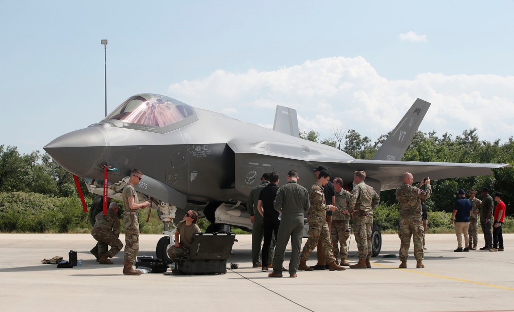 Military personnel work near F-35 fighter jet.