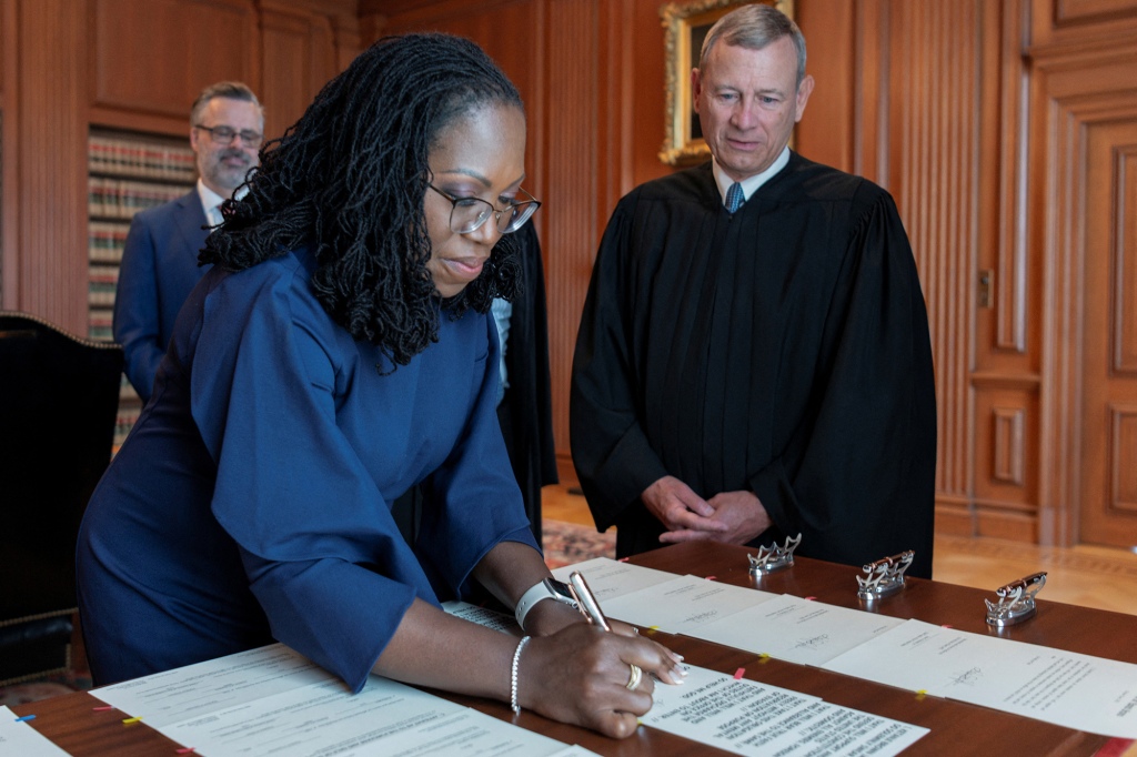Justice Ketanji Brown Jackson signs her oaths of office as her husband Patrick and Supreme Court Chief Justice John Roberts look on.