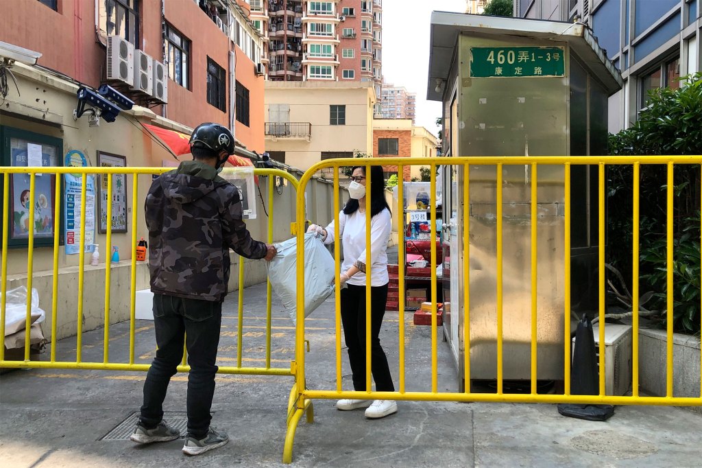 A woman wearing a face mask reaches through a barricade to receive a delivery package in Shanghai.