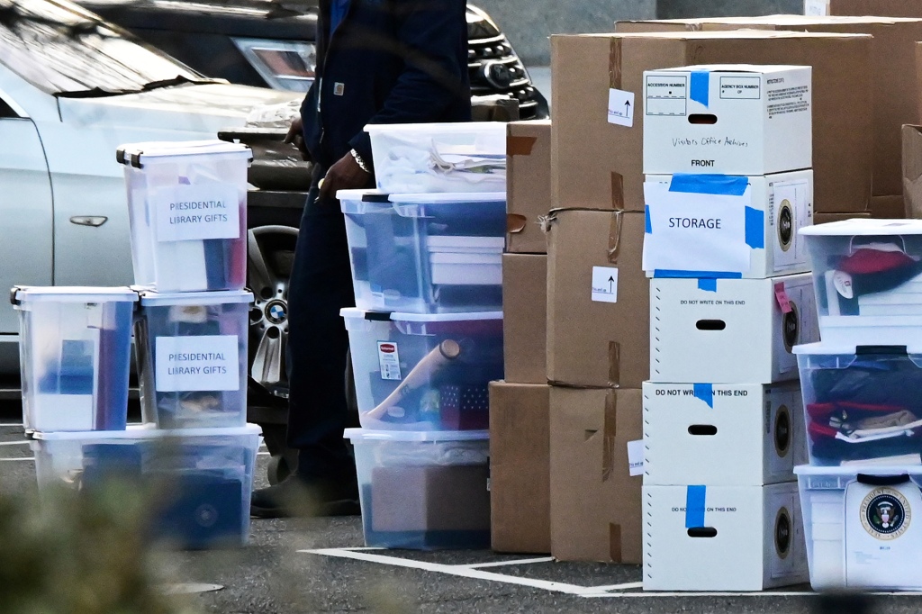 Plastic and carboard boxes, including two labeled "presidential library gifts" are piled high on roadway.