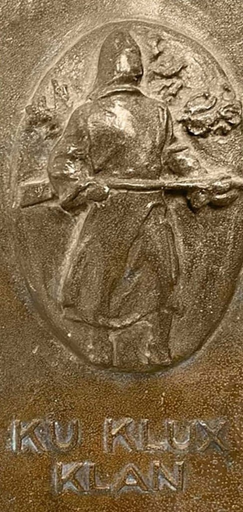 A Klansman brandishes a gun in the KKK plaque.
